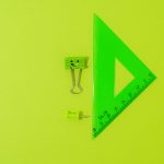 Green binder clip, push pin, and triangle ruler on vibrant backdrop, perfect for school or office themes.